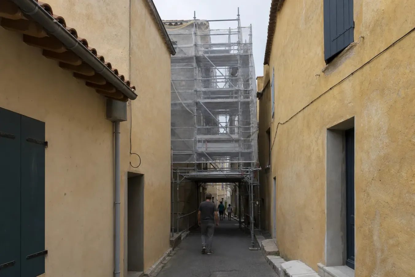 Échafaudage roulant monté dans une rue de trois mètres à peine entre deux façades ocre, passage piéton protégé au pied