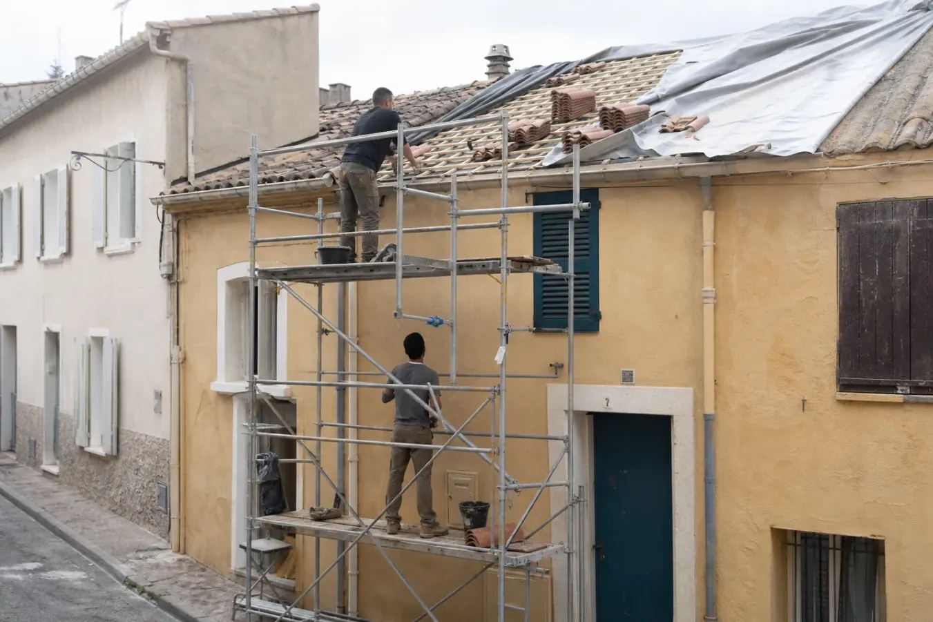 Échafaudage roulant arrimé à la façade d’une maison de ville dans une rue étroite du Midi, tuiles neuves en attente sur la plateforme