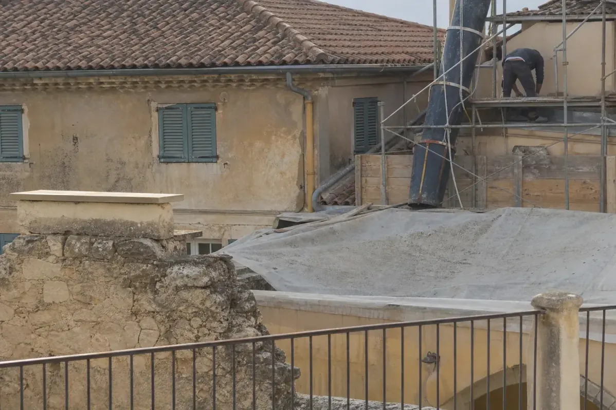 Bâches et planches protégeant la terrasse d’un voisin et un mur de cour pendant des travaux de toiture, goulotte à gravats en place