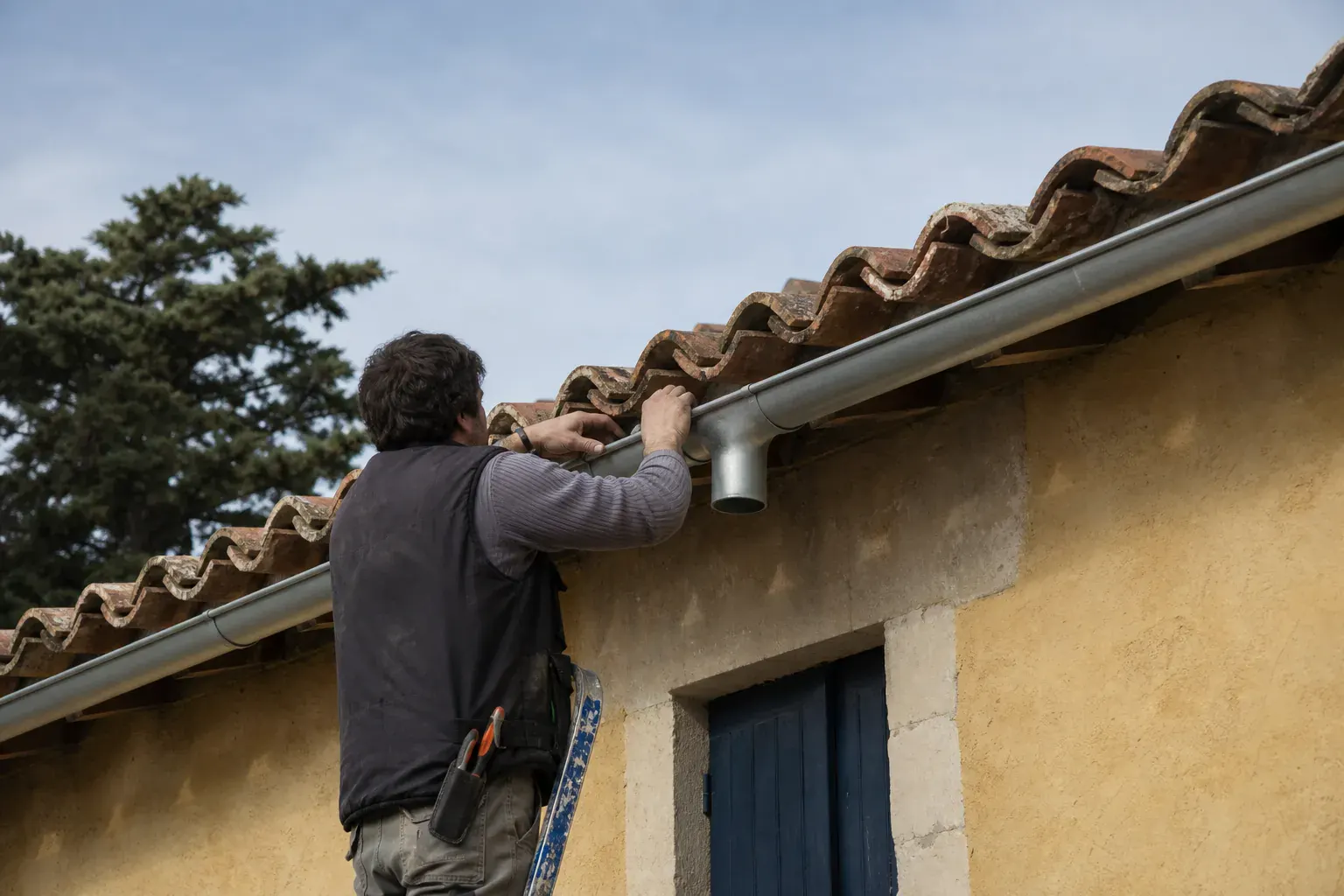 Gouttière demi-ronde en zinc fixée sur crochets le long d’un égout de toit, naissance de descente en place sur façade ocre